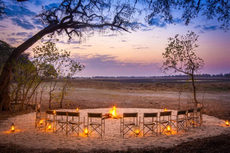 A fire lit boma with seating overlooking the plains at Kwara Camp, Botswana.