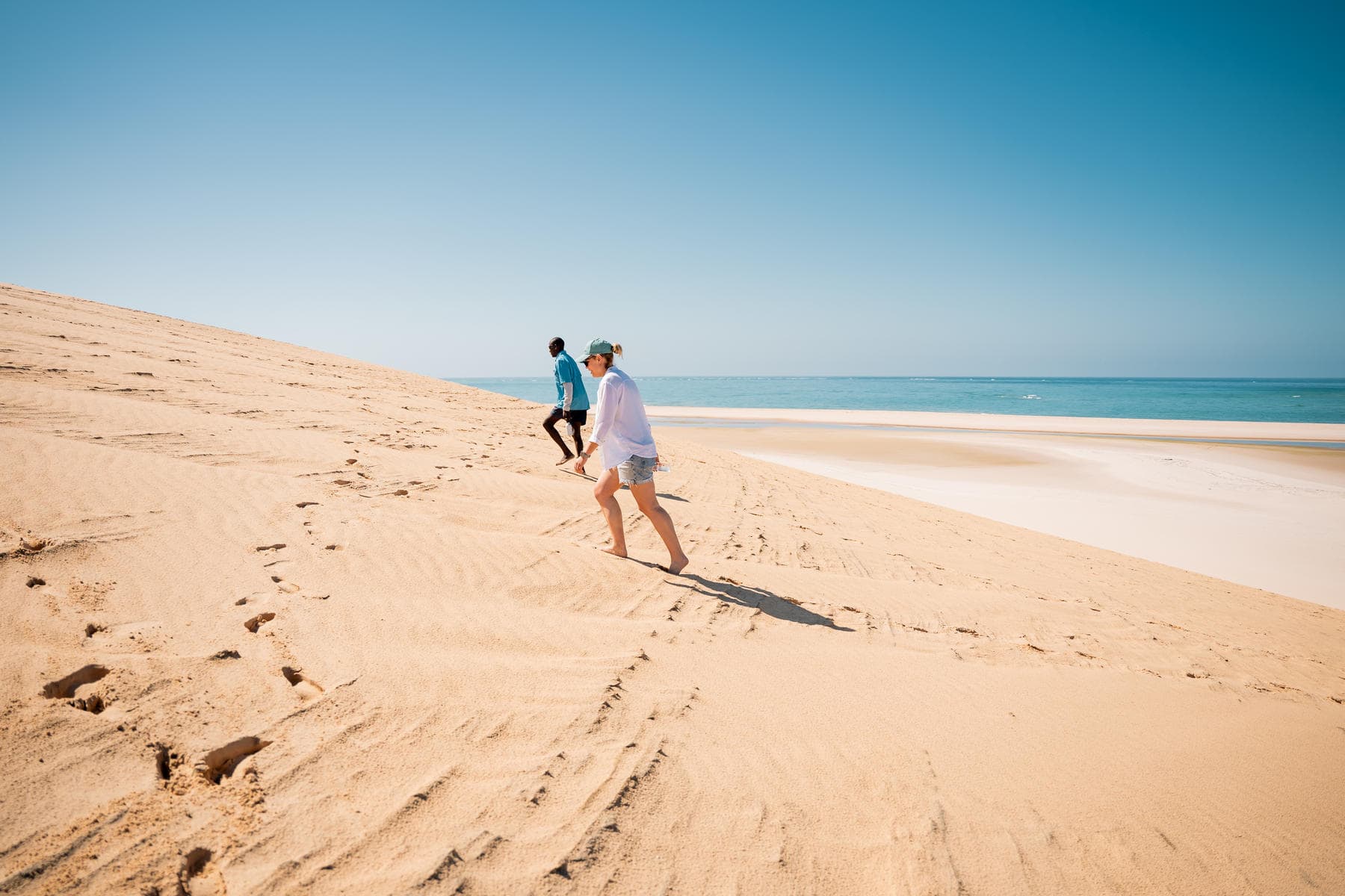 Two travellers climbing a sand dune in the Bazaruto Archipelago.
