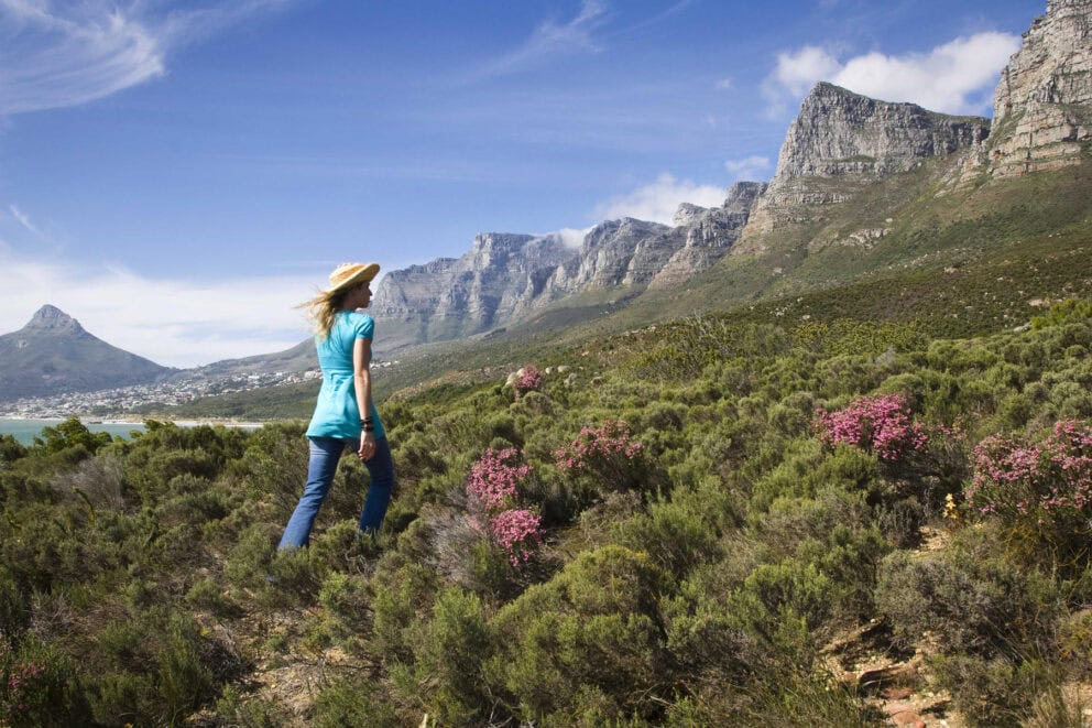 A woman walking among the flora with the Twelve Apostles Mountain Range as a backdrop at the Twelve Apostles Hotel & Spa, Cape Town.