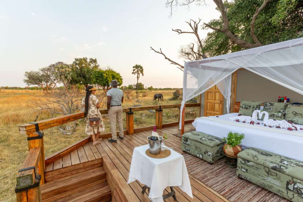 A couple standing on an elevated sleepout deck, admiring the views of the floodplains at Camp Okavango in the Okavango Delta, Botswana.