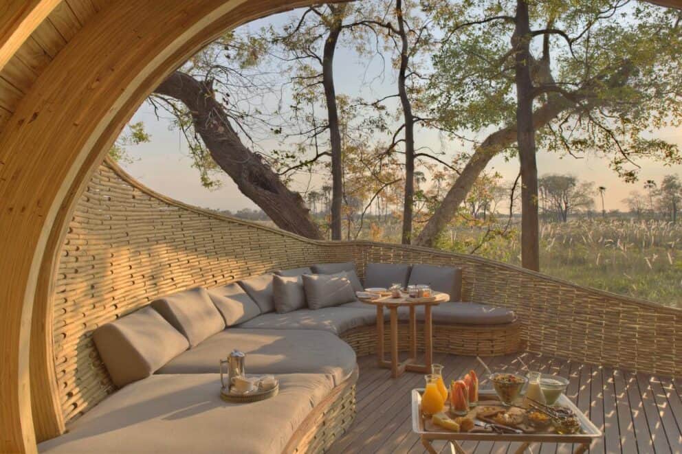 A breakfast nook at sunrise with cushioned seating overlooking the open plains at Sandibe Okavango Safari Lodge, Botswana.