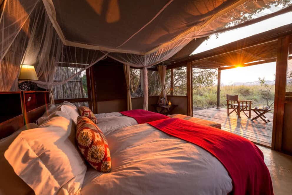 Interior bedroom view with the sun streaming in over the luxury bed at Busanga Bush Camp, Zambia.