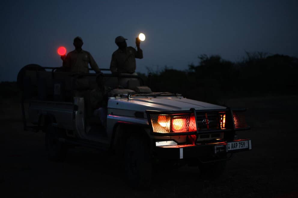 Guides shining spotlights in the dark from a safari vehicle at Puku Ridge Camp, Zambia.