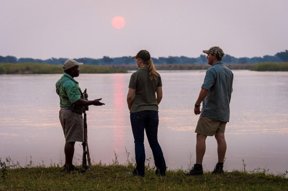 Guests on a guided walking safari standing by a riverbank near Ruckomechi in Mana Pools National Park, Zimbabwe.