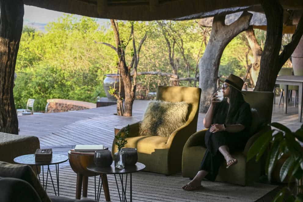 Tourist relaxing in a comfy chair on the outdoor deck overlooking the African bush at Kopano Lodge, Madikwe.