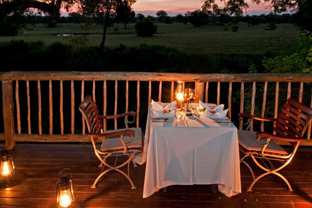 A private dinner on an elevated deck at sunset, surround by candlelight overlooking the African bush at Sabi Sabi Selati Camp in Sabi Sands Nature Reserve, South Africa.