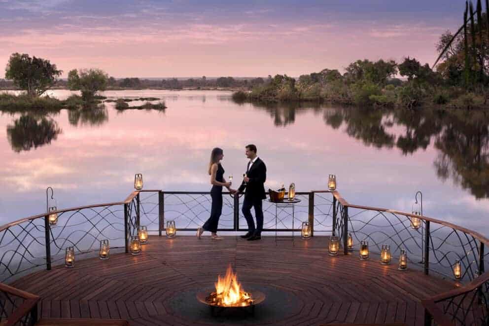 A couple on the deck at Thorntree River Lodge, a luxury safari lodge, overlooking the Zambezi at sunset.