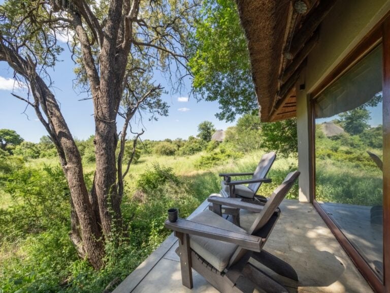 View of the bushveld from a private bedroom suite deck, featuring two armchairs at Kambaku River Sands, South Africa.