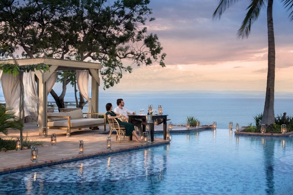 A couple relaxing in comfy wooden chairs by the pool that overlooks Lake Kariba at Bumi Hills Safari Lodge, Zimbabwe.