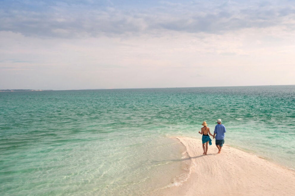 Couple holding hands while walking on the beach during the day