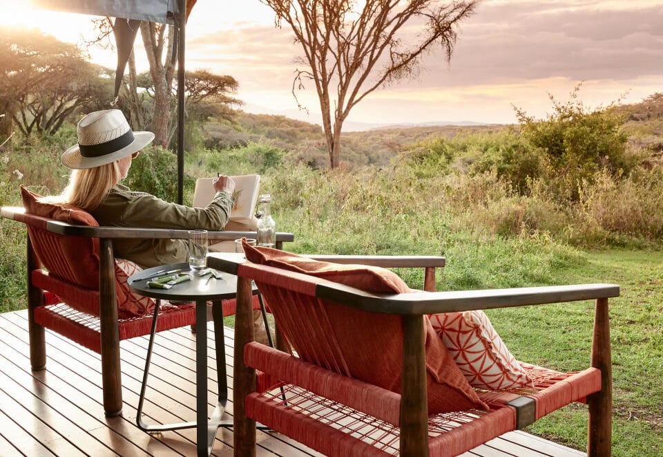 Woman on a deck at a safari camp. Opt for khaki, olive green, brown, grey, or stone-coloured clothing for your Tanzania safari packing list