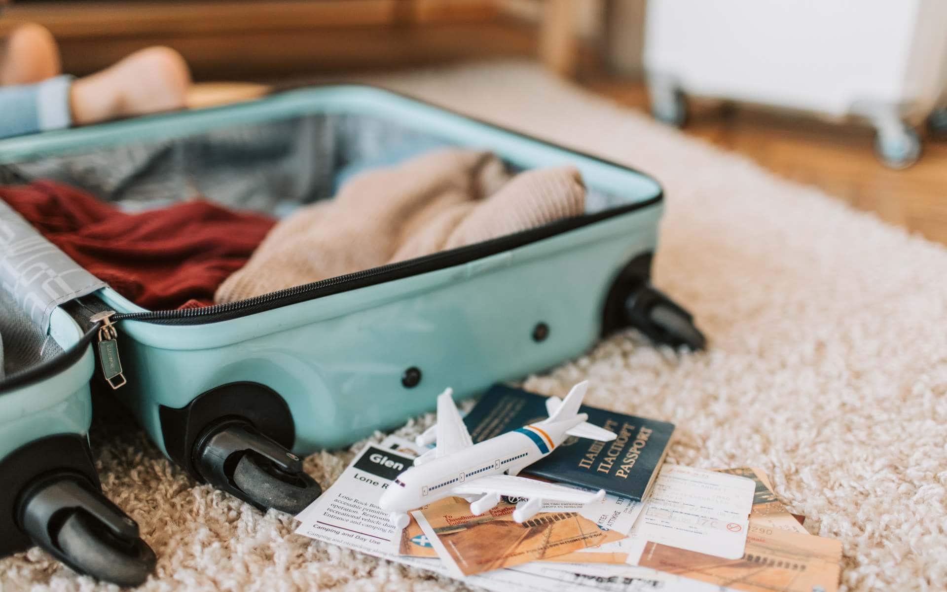 Shot of an open teal suitcase on a bed packed with various travel essentials