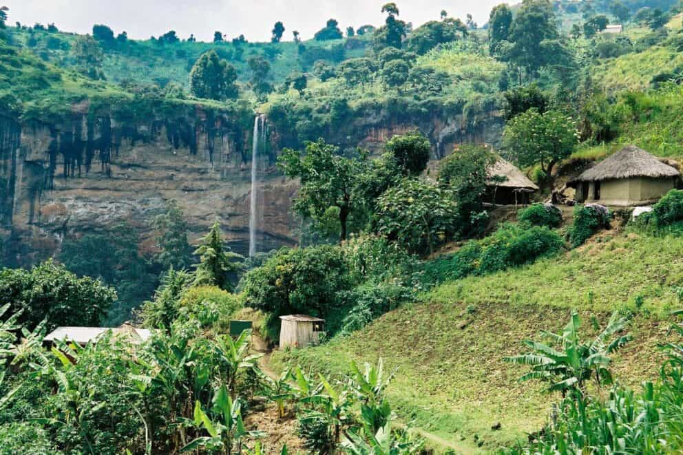 A landscape of a waterfall, rolling green hills and traditional huts.