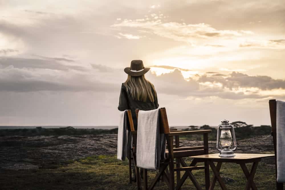 Woman watching the sunset in the Serengeti. There are few must-haves to pack with you on your Tanzania safari packing list.