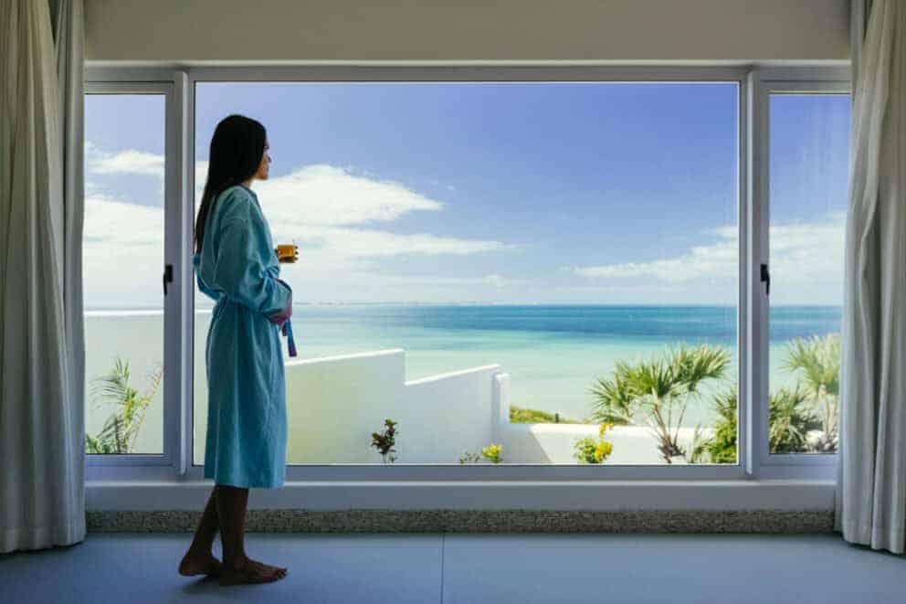 A guest standing by a large Balcony door admiring ocean views in Vilanculos, Mozambique.