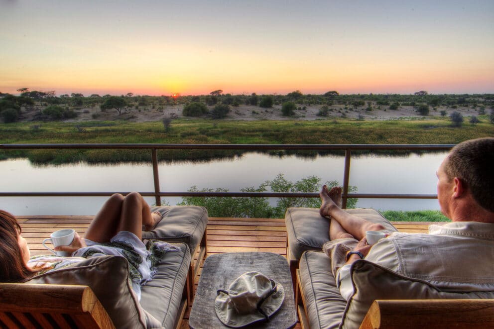 A couple relaxing on deck loungers on an elevated wooden deck overlooking the Boteti River at Leroo La Tau, Botswana.