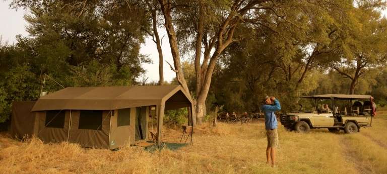 Traveller looking through binoculars for birds at a tented camp