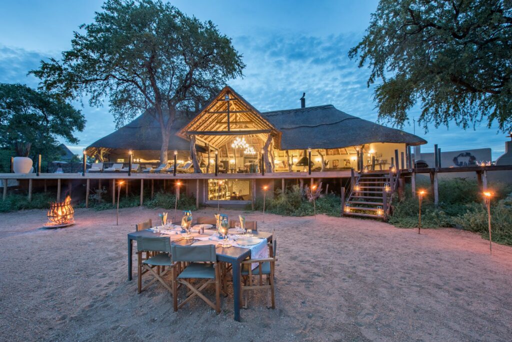 A view of Kambaku Safari Lodge in Kruger as the sun is setting, featuring a candlelit dining area .