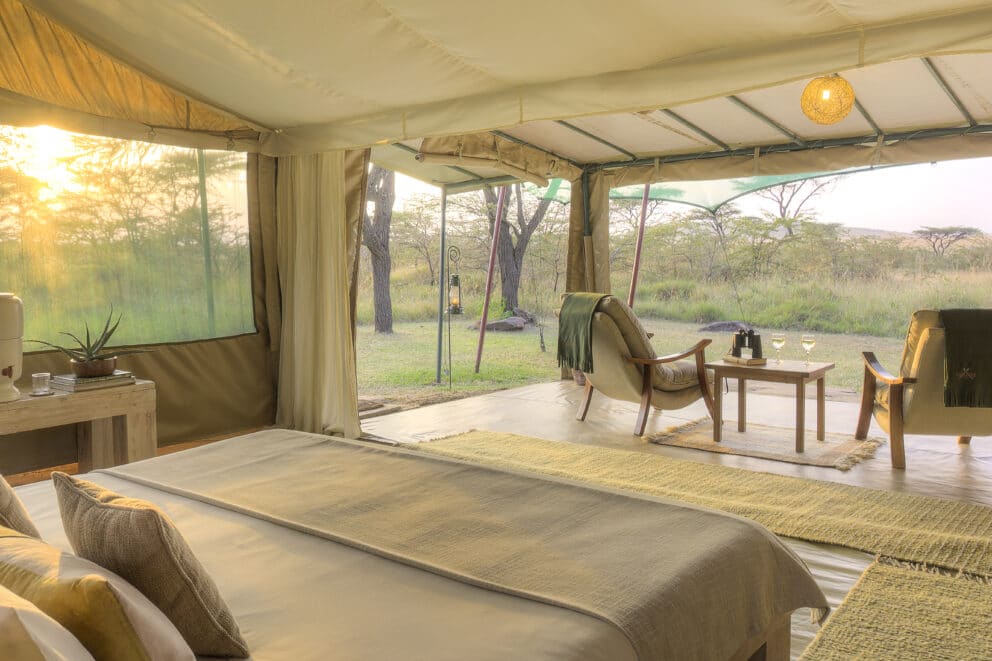 View of the bedroom tent, featuring two armchairs on a private deck overlooking the open Masai Mara plains at Kicheche Mara North, Kenya.