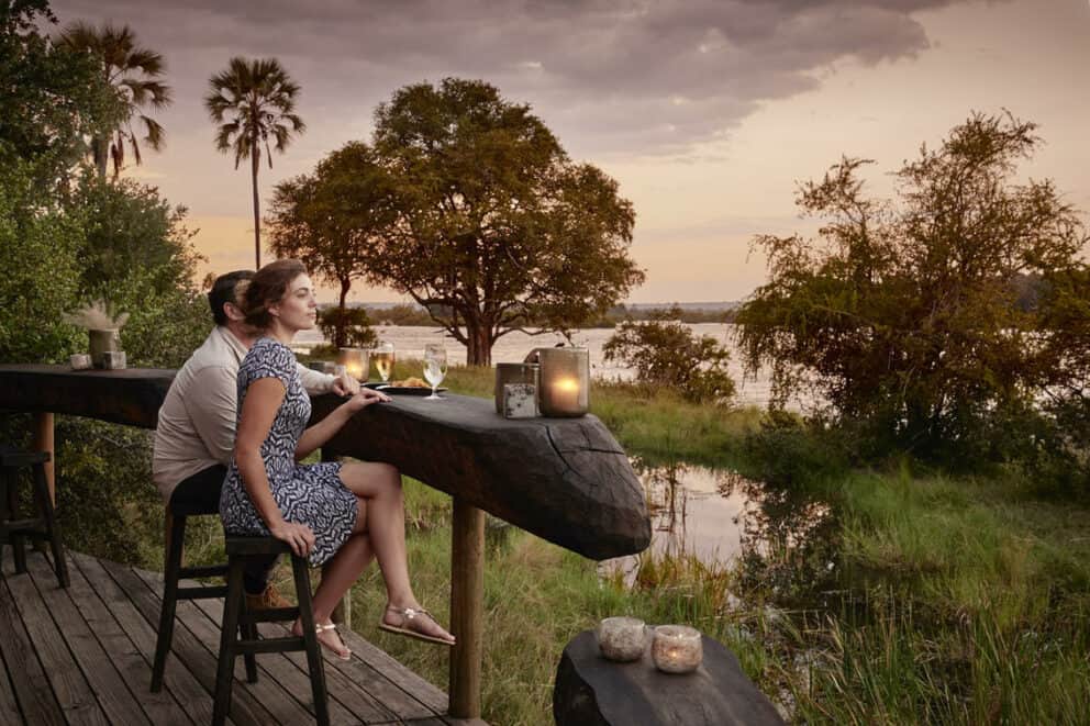 A couple sitting on a wooden deck overlooking the African landscape at Victoria Falls River Lodge in Victoria Falls, Zimbabwe.