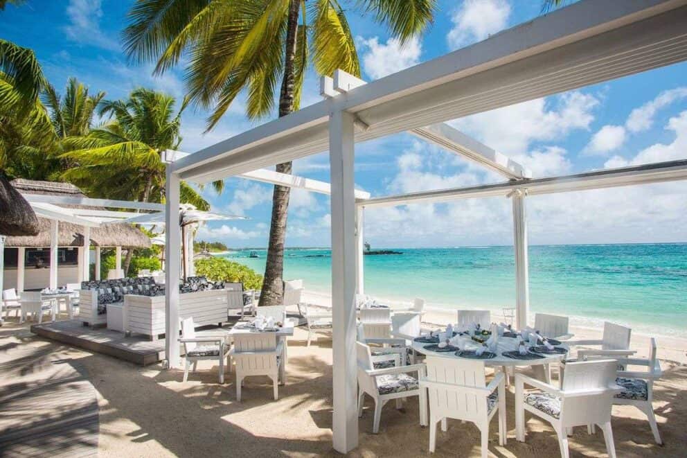 View of the Indian ocean from the sea side seating area, featuring comftable white-washed wooden cushioned chairs and tables on the shore at Constance Belle Mare Plage Resort, Mauritius.