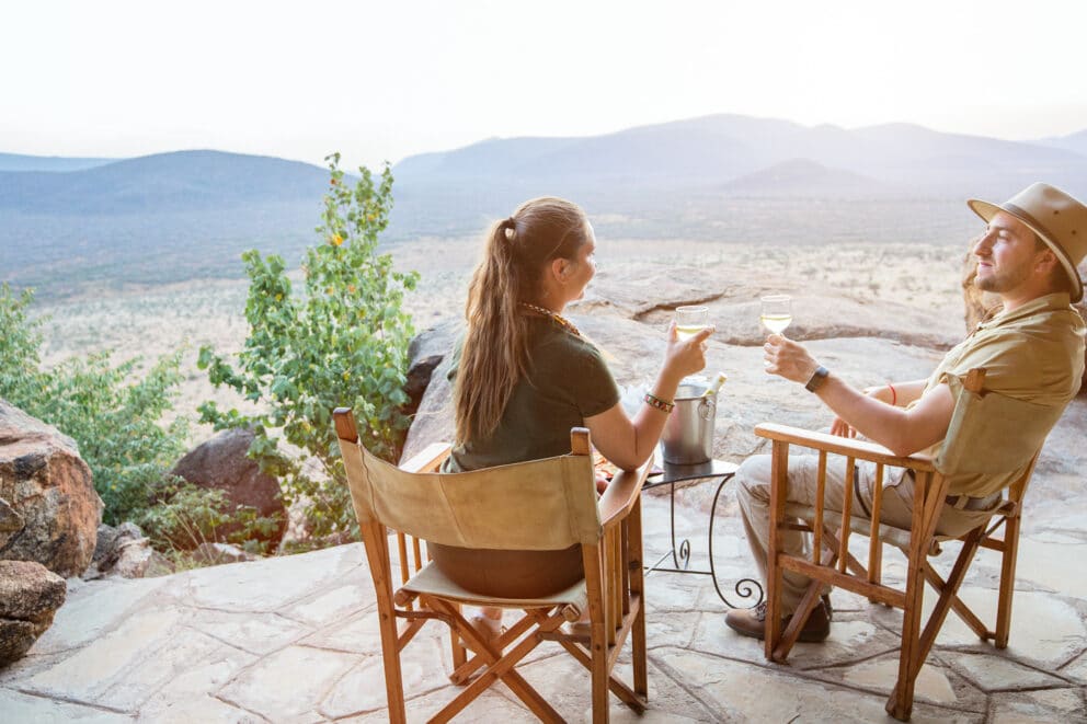 Couple on honeymoon enjoying a drink and the view from a luxury safari lodge in Kenya.