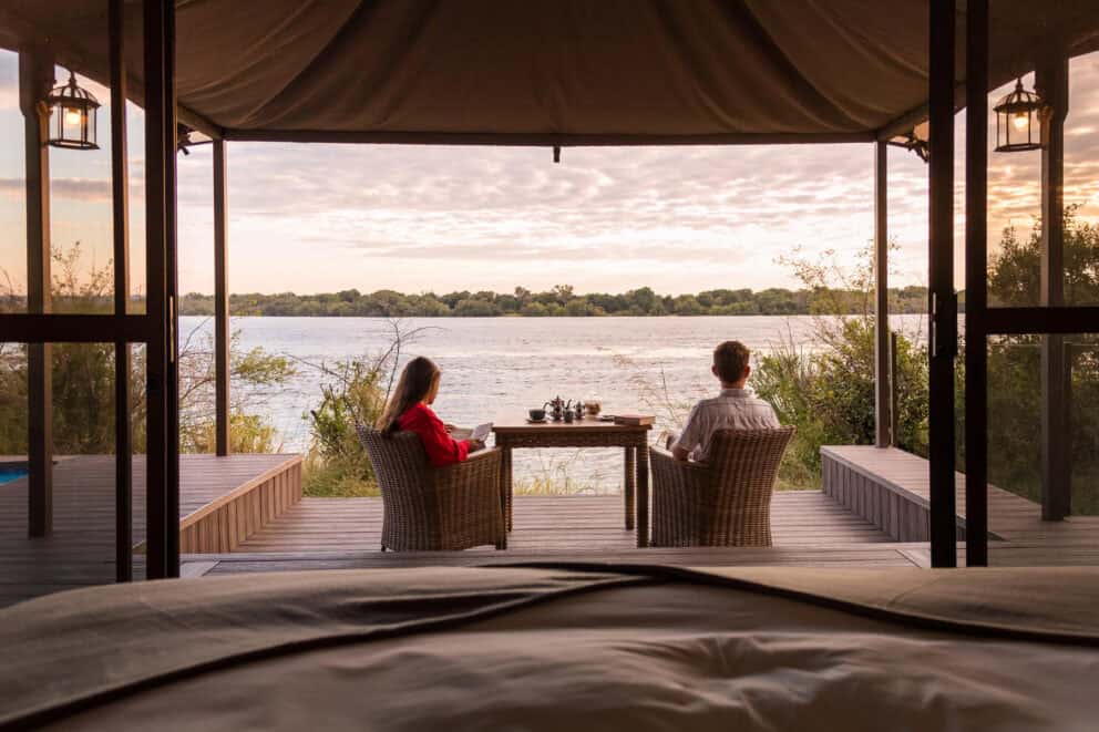 A couple sitting in comfy armchairs on a private deck looking out over the Zambezi River at Old Drift Lodge, Zimbabwe.