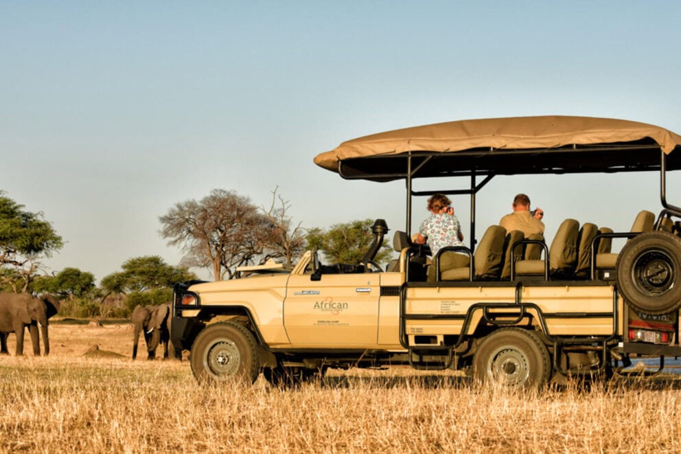 Guests on a game in a safari vehicle observing elephants in the distance near Somalisa Expeditions in Hwange National Park, Zimbabwe.