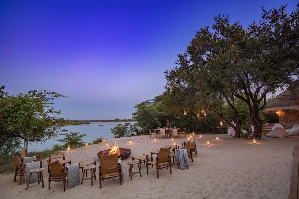 View of the lit fire pit on the sandy banks of the Zambezi River at Mpala Jena Camp, Zimbabwe.