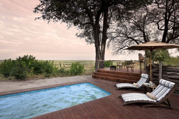 Wooden pool deck at Linyanti Bush Camp featuring sun loungers overlooking the African landscape.