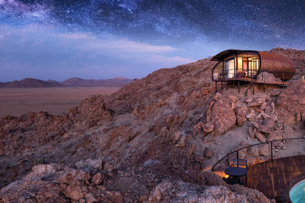 A view of the suite nestled on the rocks and a walkway leading to the plunge pool deck under a starry sky at Desert Whisper, Namibia.