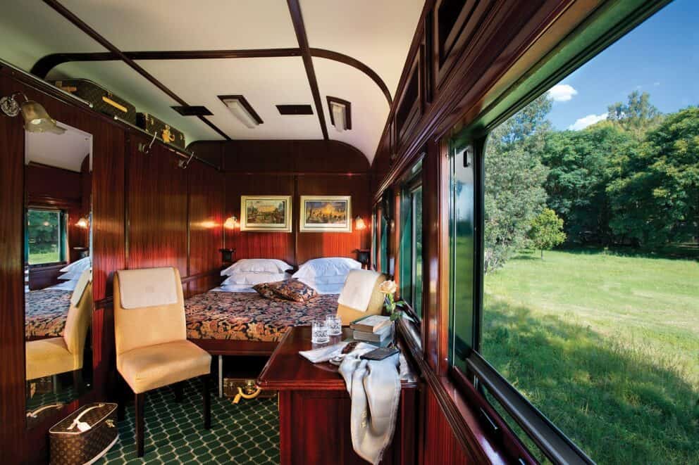 A Rovos Rail luxury cabin with a double bed and a view of the landscape.