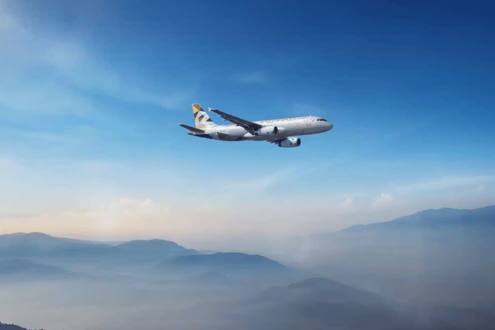 Etihad Airways plane flying across blue sky over mountains