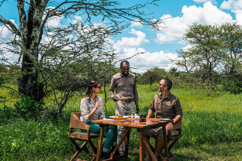 Guests enjoying a bush lunch at a set dining table under the lush forest canopy near Lemala Osonjoi Lodge on the Ngorongoro Crater Rim, Tanzania.