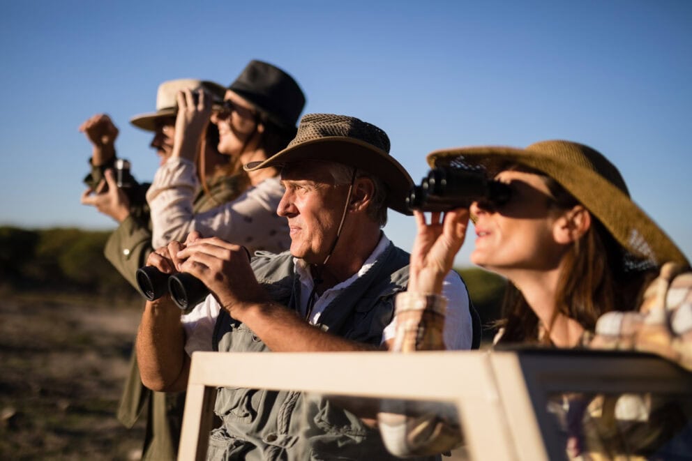 Group of friends looking through binoculars during safari vacation in South Africa. Photo: Getty Images