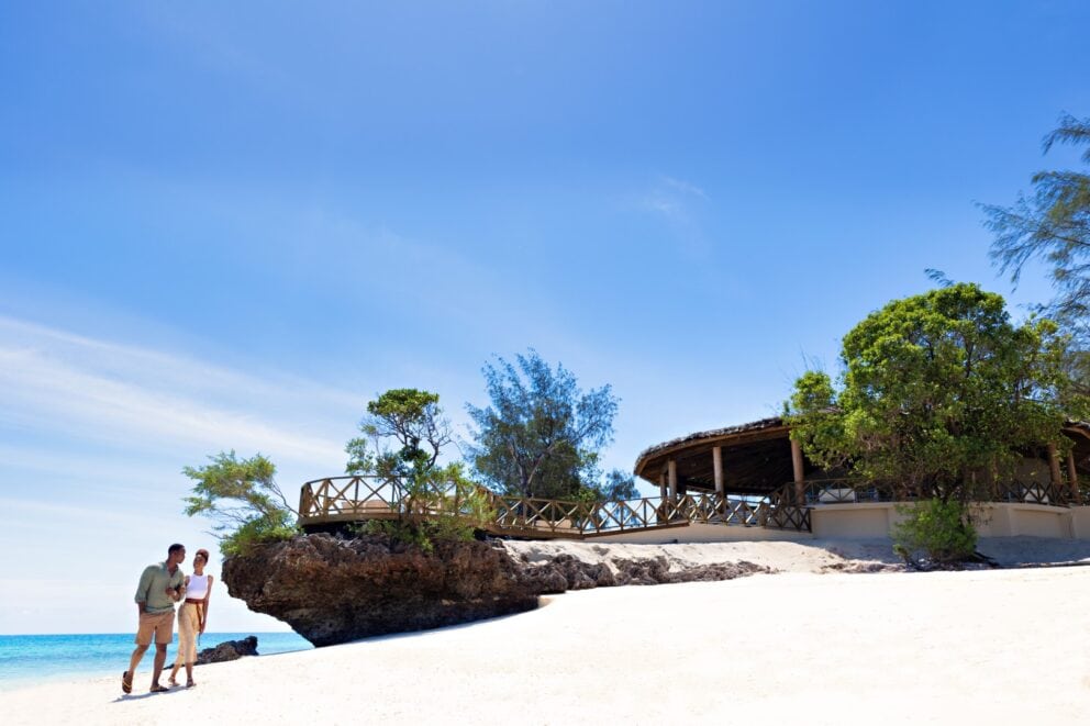 A couple walking on a pristine beach with the blue ocean in the background at Bawe Island, Zanzibar.