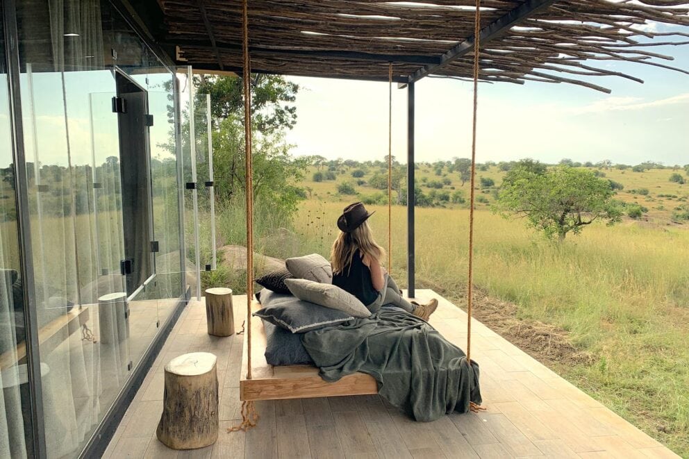 A woman sitting on a swing bed suspended over a wooden deck under a verandah at Nimali Mara, Tanzania.
