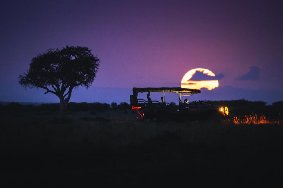 A safari vehicle at dusk with the sun setting in the background at Emboo Camp, Kenya.