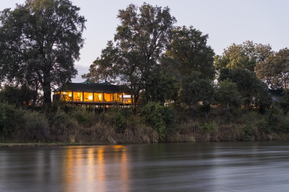 Exterior view at dusk of a luxury lantern lit tented suite along the Zambezi River bank at Amanzi Camp, Zambia.