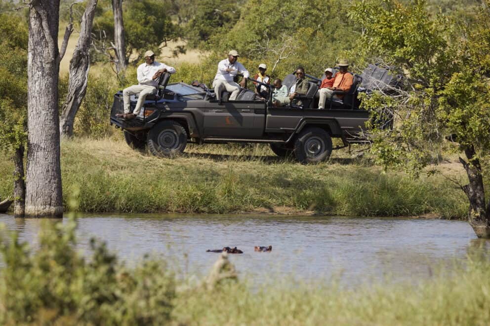 Family on a game drive watching two hippos in the water atSabi Sands Private Game Reserve.