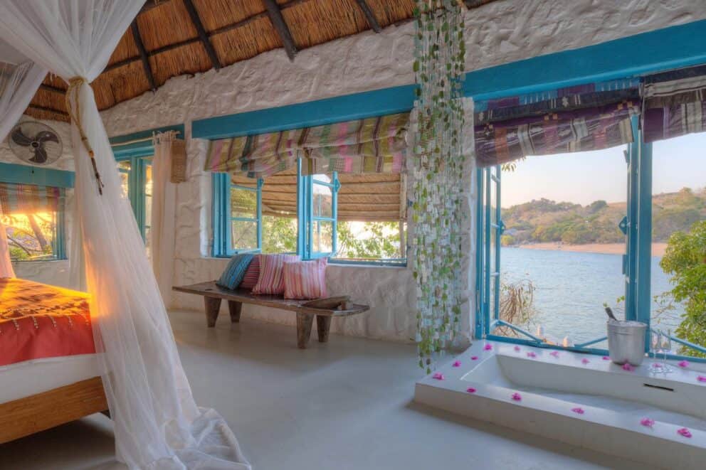 View from a luxury bedroom at Kaya Mawa looking out over the clear blue waters of Lake Malawi through an open window.