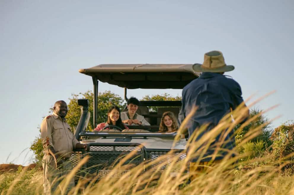 A dad taking a photograph of his family in a safari vehicle with their guide at Chobe Chilwero Lodge, Botswana.