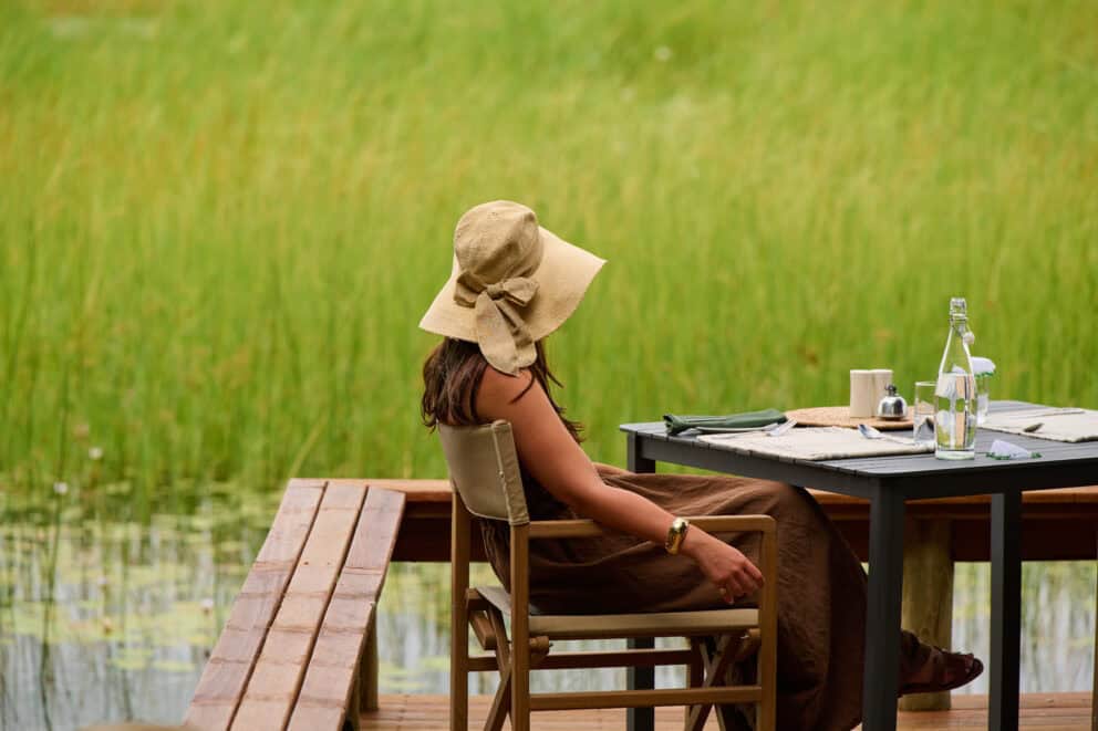 A woman sitting at a table outdoors overlooking the green landscape at Sediba Sa Rona, Botswana.