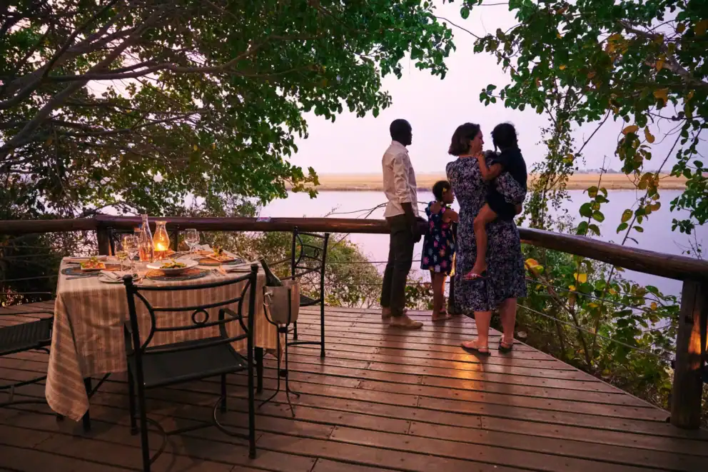 A family on an elevated wooden deck at sunset overlooking the Chobe River at Chobe Game Lodge, Botswana.