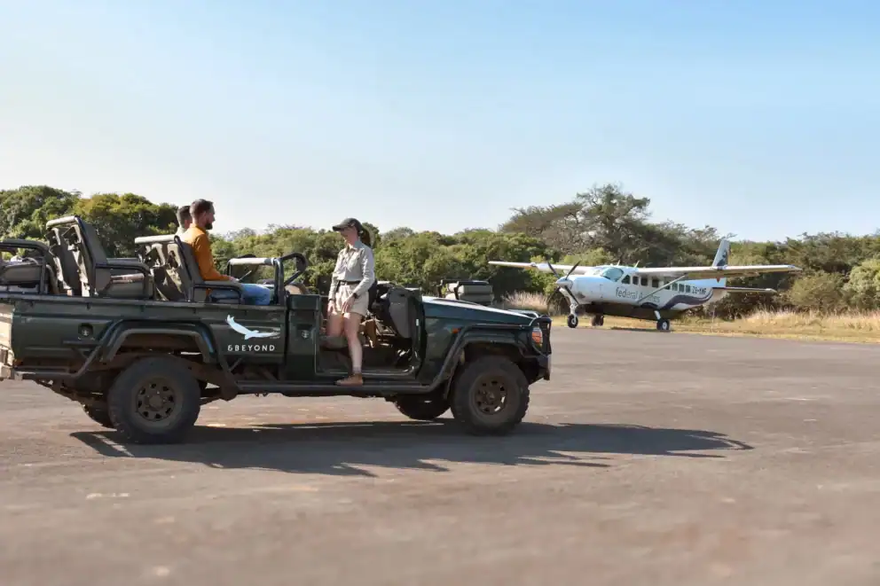 Guests in a safari vehicle with their guide at a luxury game reserve's private airstrip in South Africa, with a FedAir bush plane in the distance.