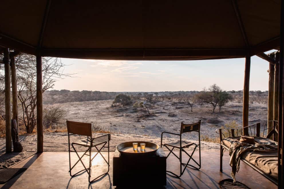 View from the tented suite deck, featuring two armchairs and a lit fire at Meno a Kwena, Botswana.