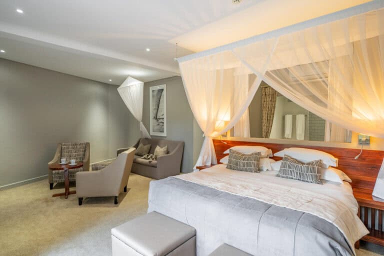 View of the family room, featuring a canopied bed with luxury insect netting draped over and comfortable armchairs at Chobe Safari Lodge, Botswana.