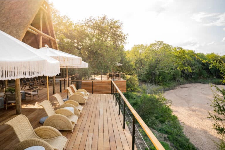 View of the riverbed from the elevated deck with cushioned seating under umbrellas at Thornybush Game Lodge, South Africa.