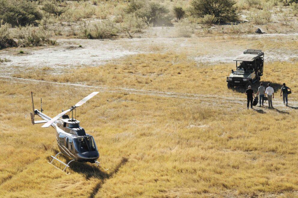 A stationary helicopter with a safari vehicle parked in the distance.