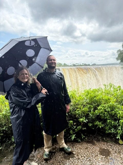 Tourists standing before Victoria Falls with a big umbrella and raincoats completely soaked by the spray.